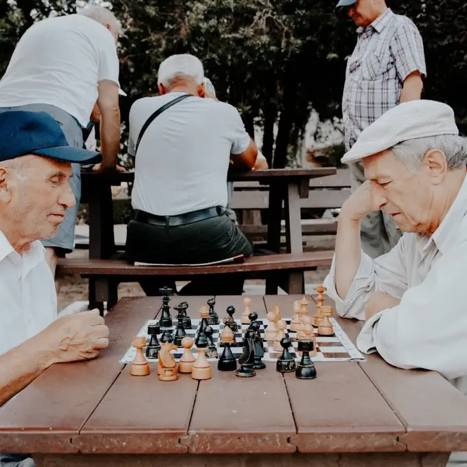 Two elderly men playing chess outdoors at a park bench, focused on the game.